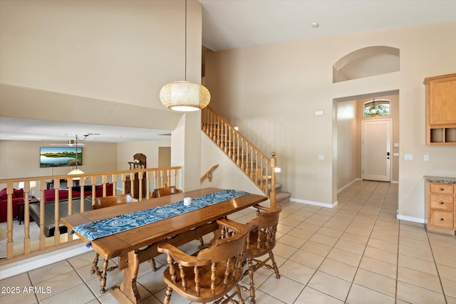 dining area with light tile patterned floors, baseboards, a high ceiling, and stairs