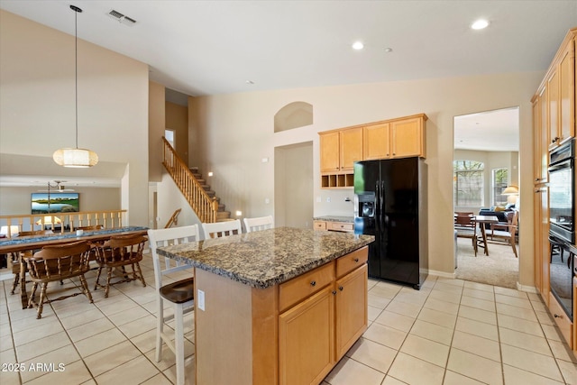 kitchen featuring light brown cabinets, a kitchen bar, a center island, light tile patterned floors, and black fridge