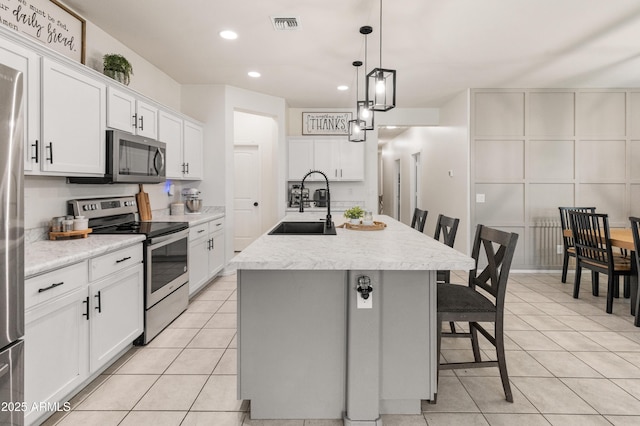 kitchen with a kitchen bar, a center island with sink, a sink, appliances with stainless steel finishes, and light tile patterned floors