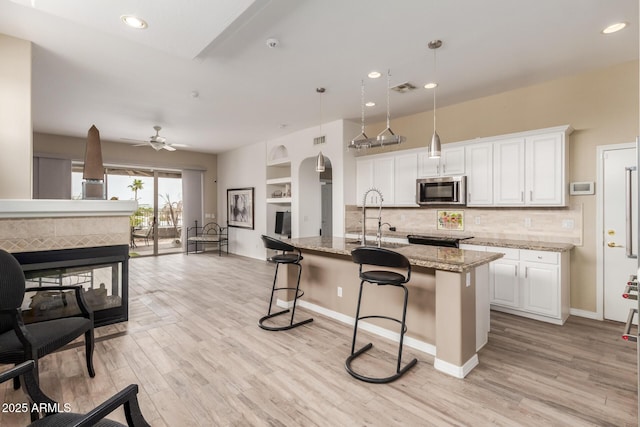 12841 N 19th St, Phoenix, AZ 85022 - kitchen with white cabinetry, stainless steel microwave, a breakfast bar, light wood-style floors, and light stone counters