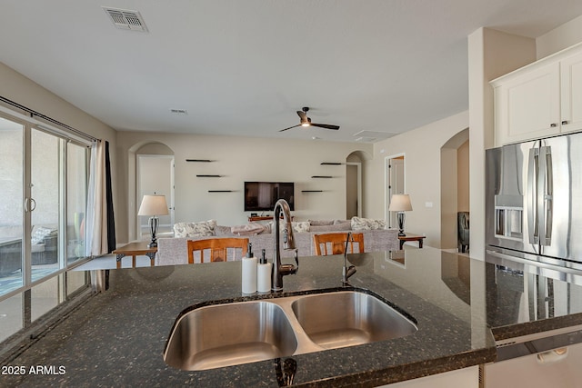 kitchen featuring white cabinets, stainless steel fridge, dark stone counters, and a sink