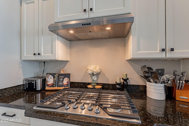 kitchen with white cabinetry, stainless steel gas stovetop, under cabinet range hood, and dark stone countertops