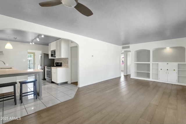 unfurnished living room with visible vents, light wood finished floors, a ceiling fan, arched walkways, and a sink