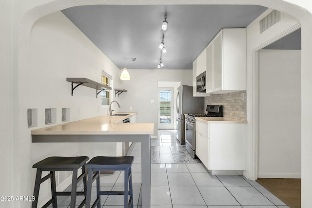 kitchen with a sink, backsplash, open shelves, a kitchen bar, and appliances with stainless steel finishes