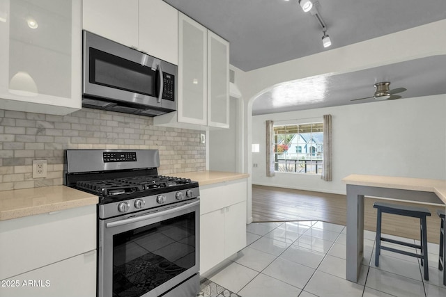 kitchen with light tile patterned flooring, light countertops, white cabinets, appliances with stainless steel finishes, and arched walkways