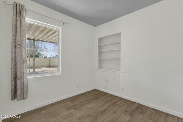 empty room featuring built in features, baseboards, and wood finished floors