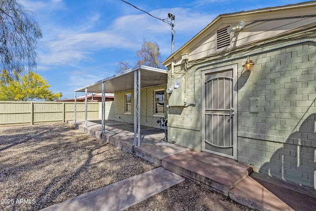 exterior space featuring concrete block siding, a carport, fence, and a patio
