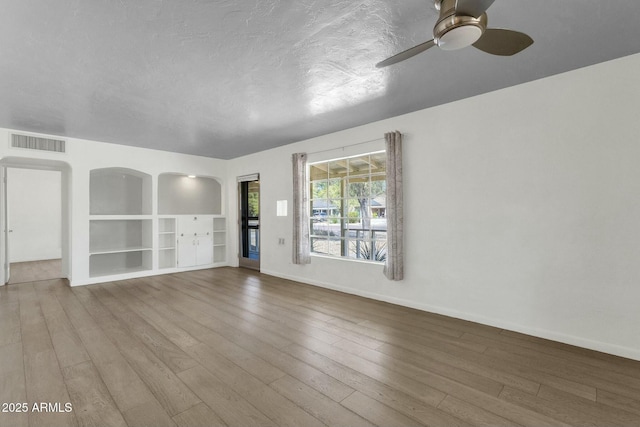 unfurnished living room featuring baseboards, a textured ceiling, hardwood / wood-style flooring, visible vents, and a ceiling fan