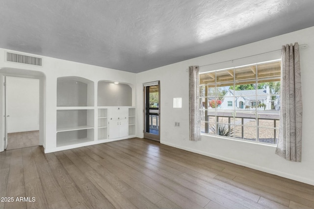 interior space featuring wood-type flooring, a textured ceiling, baseboards, and visible vents