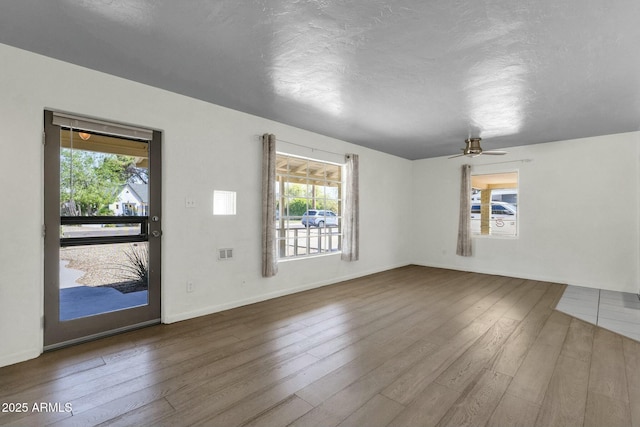 unfurnished living room with baseboards, a textured ceiling, visible vents, ceiling fan, and wood finished floors