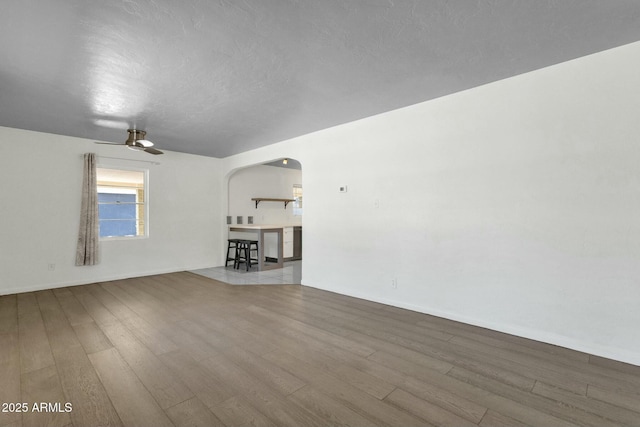 empty room featuring arched walkways, wood finished floors, ceiling fan, and a textured ceiling