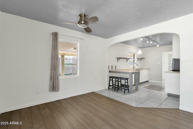 interior space featuring a sink, a ceiling fan, light wood-style flooring, baseboards, and arched walkways