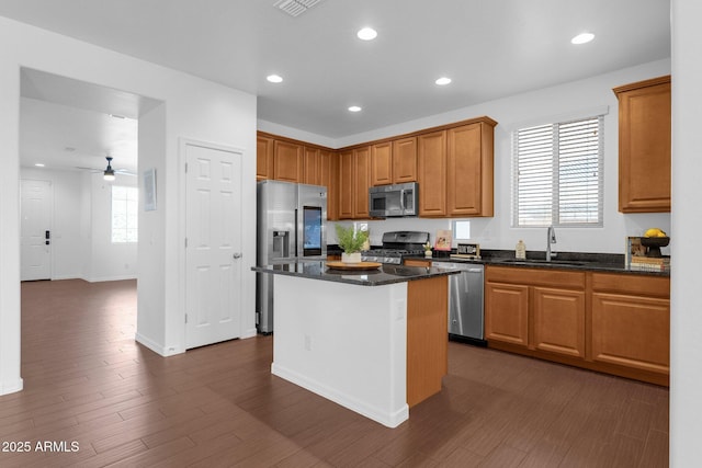 kitchen with sink, appliances with stainless steel finishes, dark stone countertops, a kitchen island, and dark hardwood / wood-style flooring