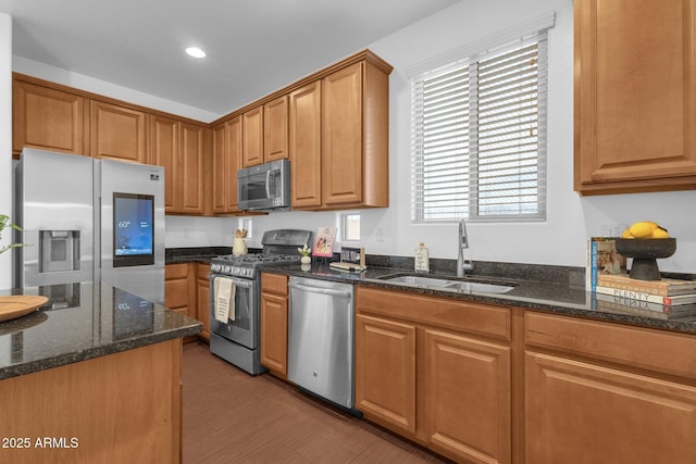 kitchen with dark stone countertops, sink, light hardwood / wood-style flooring, and appliances with stainless steel finishes