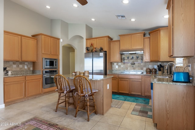 kitchen featuring appliances with stainless steel finishes, a kitchen island, light stone counters, and vaulted ceiling