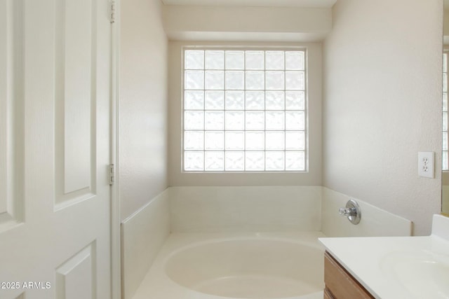 bathroom with a wealth of natural light, vanity, and a bath