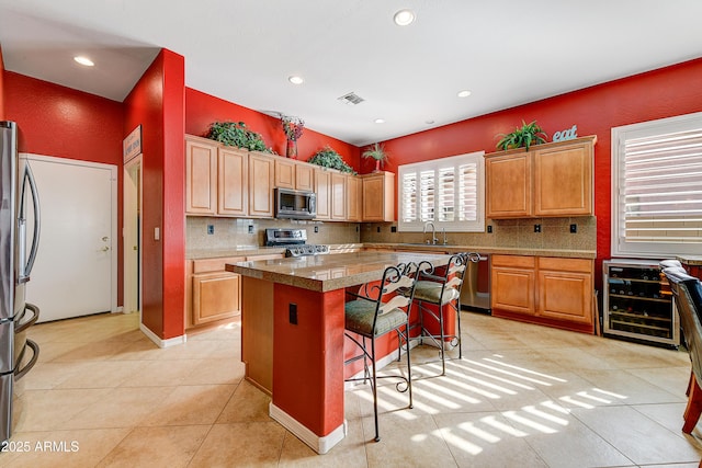 kitchen featuring a breakfast bar area, stainless steel appliances, a kitchen island, decorative backsplash, and beverage cooler