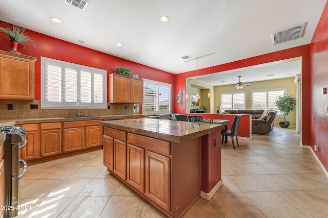 kitchen with sink, hanging light fixtures, backsplash, stainless steel range oven, and a kitchen island