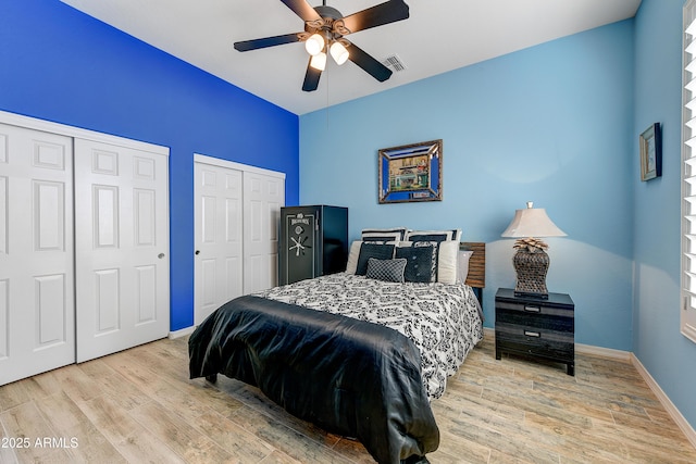 bedroom with two closets, light hardwood / wood-style floors, and ceiling fan