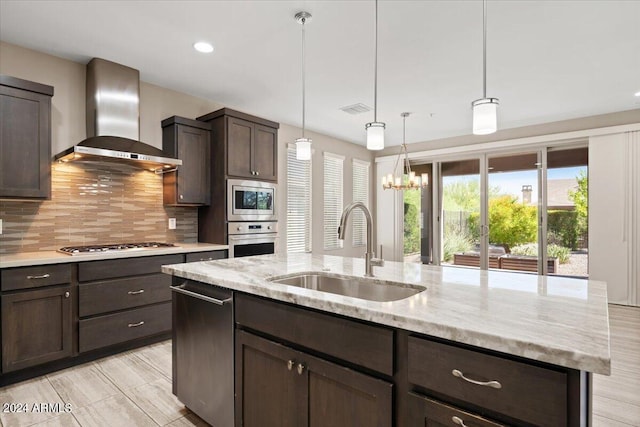 kitchen with backsplash, sink, a kitchen island with sink, appliances with stainless steel finishes, and wall chimney exhaust hood