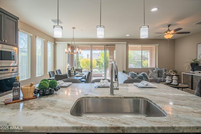 kitchen featuring stainless steel appliances, pendant lighting, light stone counters, and sink