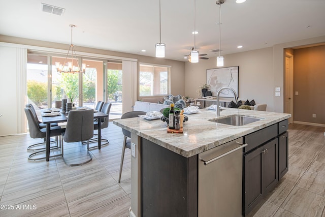 kitchen with dishwasher, a center island with sink, sink, dark brown cabinetry, and light stone countertops