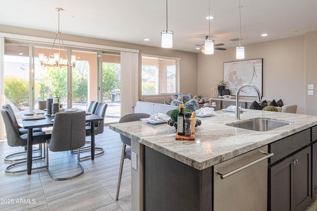 kitchen with pendant lighting, ceiling fan with notable chandelier, light stone counters, dark brown cabinetry, and sink