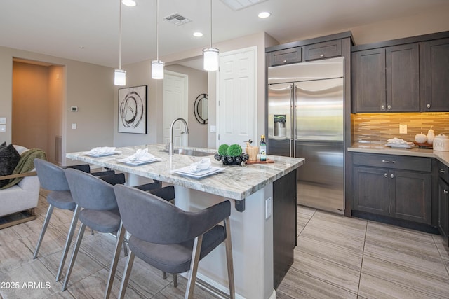 kitchen featuring built in fridge, pendant lighting, decorative backsplash, a breakfast bar, and a center island with sink