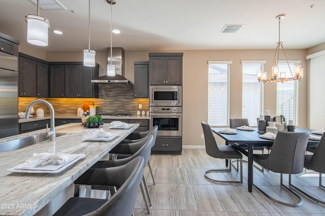 kitchen featuring decorative backsplash, dark brown cabinets, appliances with stainless steel finishes, and wall chimney exhaust hood