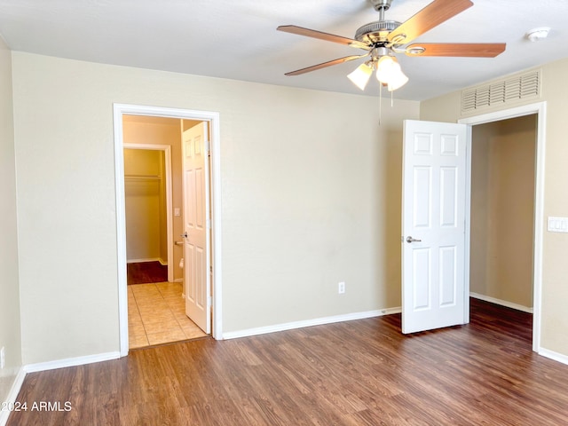 unfurnished bedroom featuring a closet, a spacious closet, ceiling fan, and dark wood-type flooring