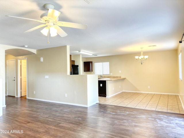 unfurnished living room with hardwood / wood-style flooring, ceiling fan with notable chandelier, and a wealth of natural light