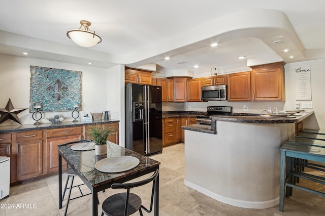 kitchen with a kitchen breakfast bar, dark stone counters, kitchen peninsula, and appliances with stainless steel finishes