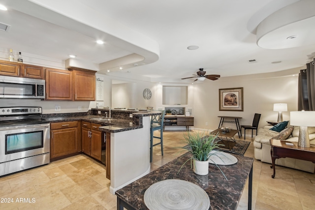 kitchen with sink, ceiling fan, a breakfast bar, appliances with stainless steel finishes, and dark stone countertops