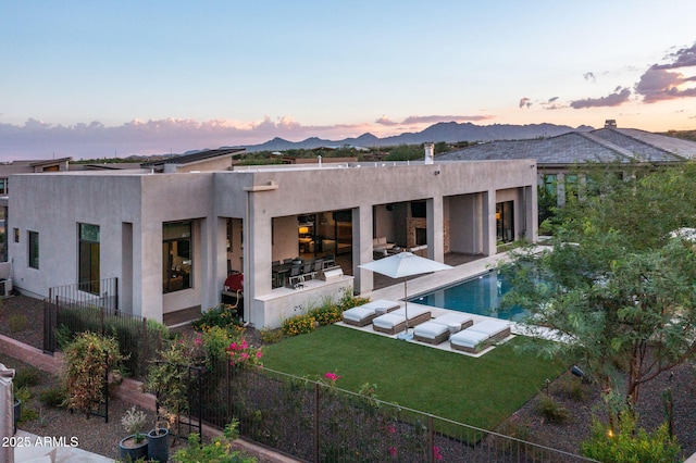 back house at dusk featuring a mountain view, a lawn, a patio area, an outdoor hangout area, and a fenced in pool