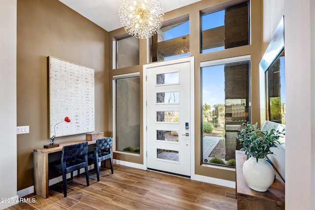 entrance foyer with a chandelier, wood finish floors, a towering ceiling, and baseboards