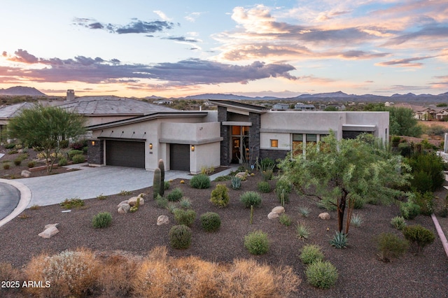 view of front of home with a garage, stone siding, decorative driveway, a mountain view, and stucco siding