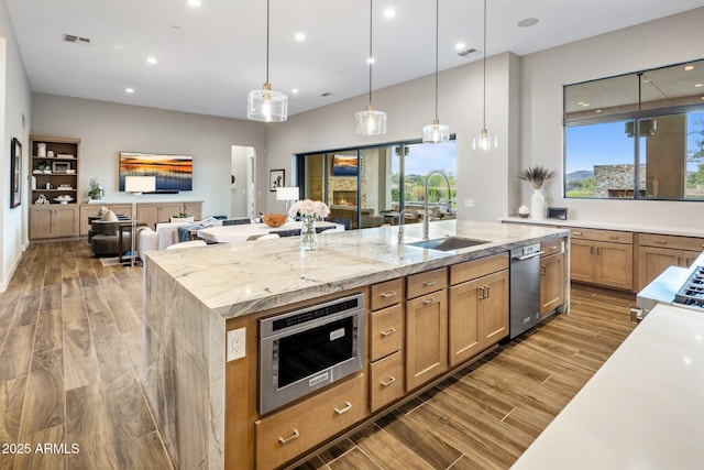 kitchen featuring light stone counters, a spacious island, wood finished floors, a sink, and decorative light fixtures