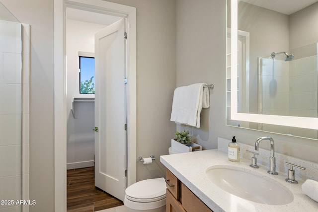 bathroom featuring toilet, a tile shower, wood finished floors, and vanity