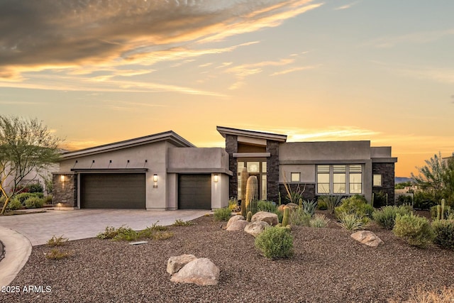 modern home with stone siding, decorative driveway, an attached garage, and stucco siding