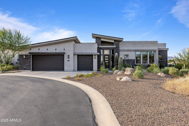 contemporary house featuring stone siding, an attached garage, driveway, and stucco siding