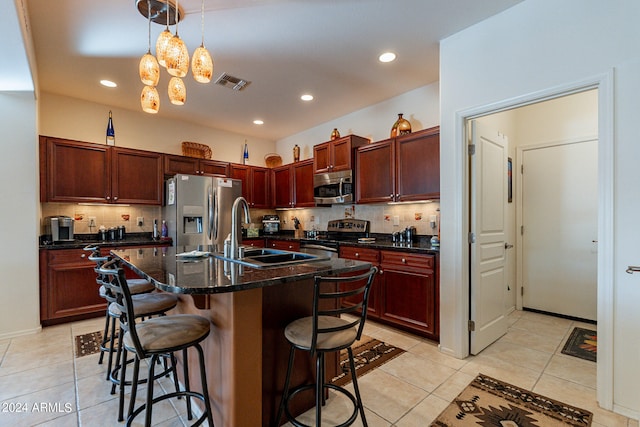 kitchen featuring sink, tasteful backsplash, a kitchen island with sink, appliances with stainless steel finishes, and a breakfast bar