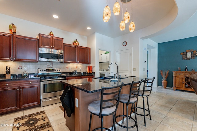 kitchen featuring pendant lighting, an island with sink, sink, backsplash, and stainless steel appliances