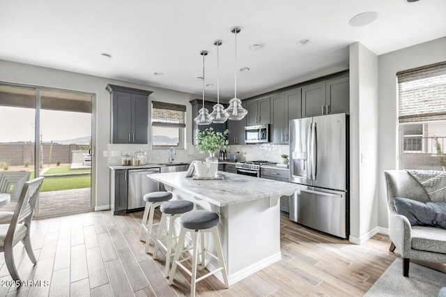 kitchen featuring decorative light fixtures, a kitchen island, gray cabinetry, a breakfast bar area, and stainless steel appliances