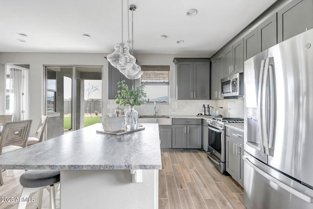 kitchen featuring decorative light fixtures, a center island, a kitchen bar, appliances with stainless steel finishes, and gray cabinetry