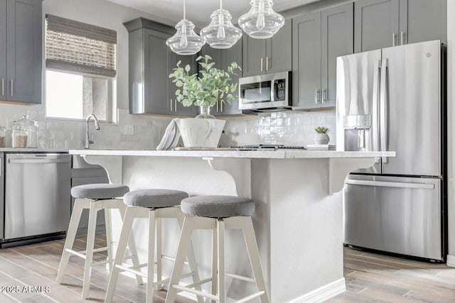 kitchen with a breakfast bar, gray cabinetry, stainless steel appliances, and light hardwood / wood-style flooring