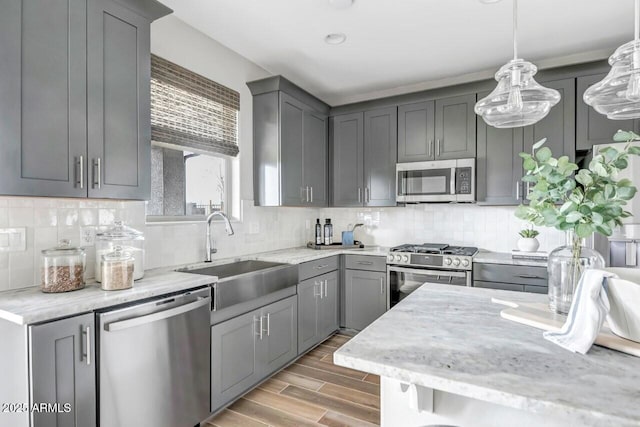 kitchen featuring gray cabinets, decorative backsplash, sink, hanging light fixtures, and stainless steel appliances