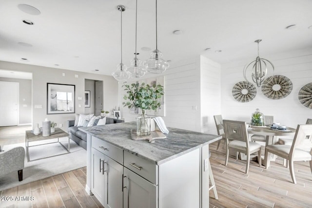 kitchen with an inviting chandelier, gray cabinets, decorative light fixtures, light stone countertops, and a center island