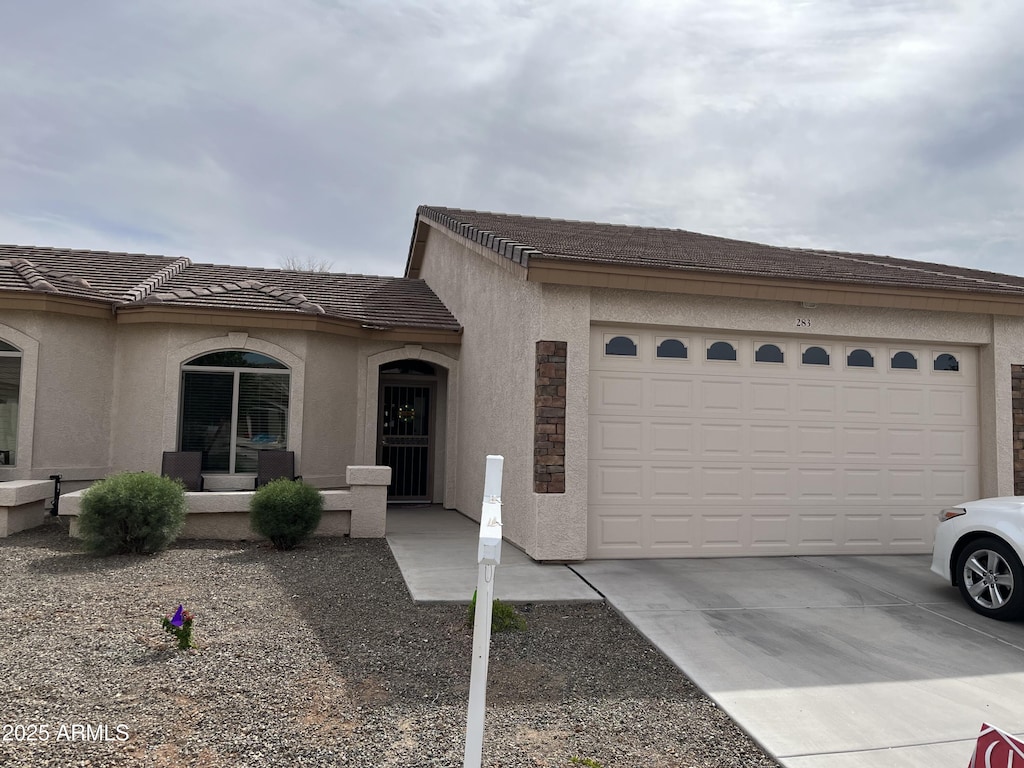 view of front of house with a porch, an attached garage, a tile roof, driveway, and stucco siding