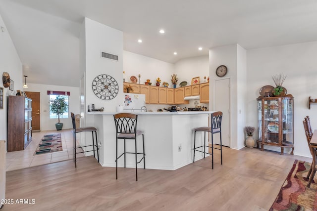 kitchen featuring high vaulted ceiling, light wood-type flooring, a kitchen breakfast bar, kitchen peninsula, and white fridge