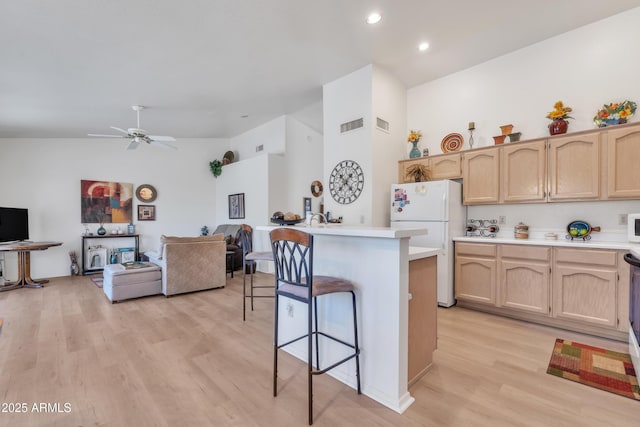 kitchen featuring a breakfast bar area, light brown cabinets, light hardwood / wood-style floors, and white refrigerator